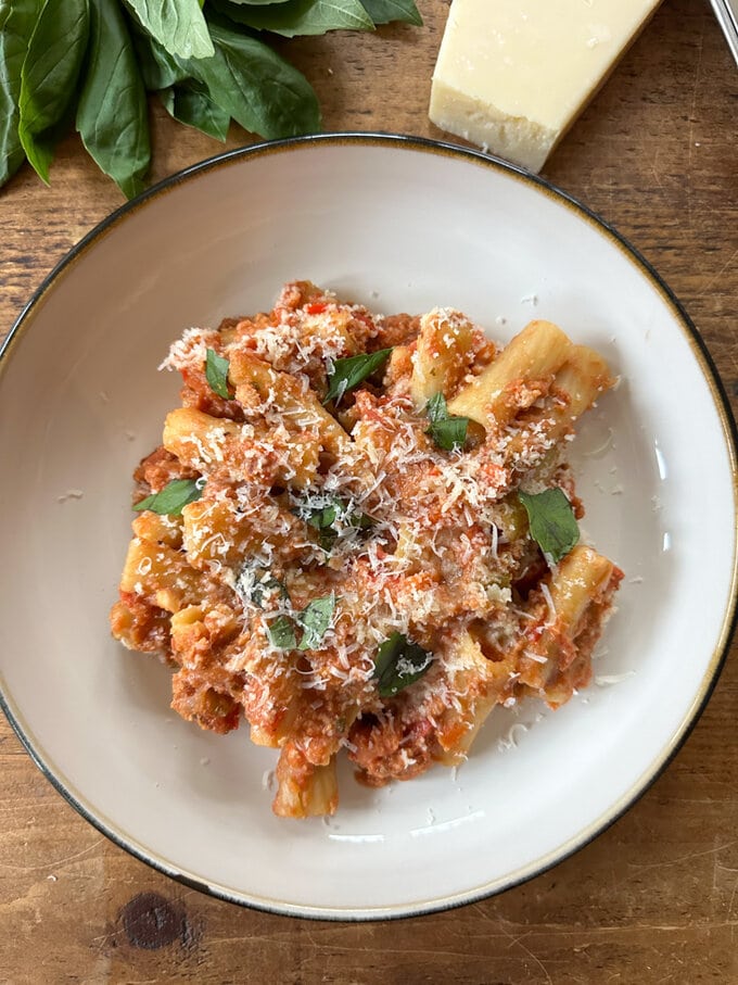 Slow Cooker Sausage Ragu served in a large white round bowl, and garnished with grated cheese and basil.