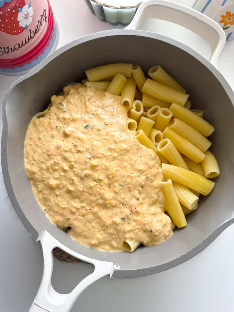 Airfryer Creamy hidden veg pasta sauce in a saucepan being mixed into tubed shaped pasta.