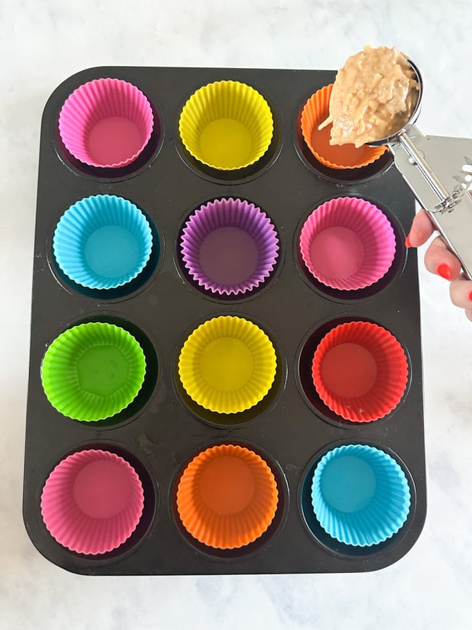Muffin mixture being added into individual cases with a ice cream scoop.