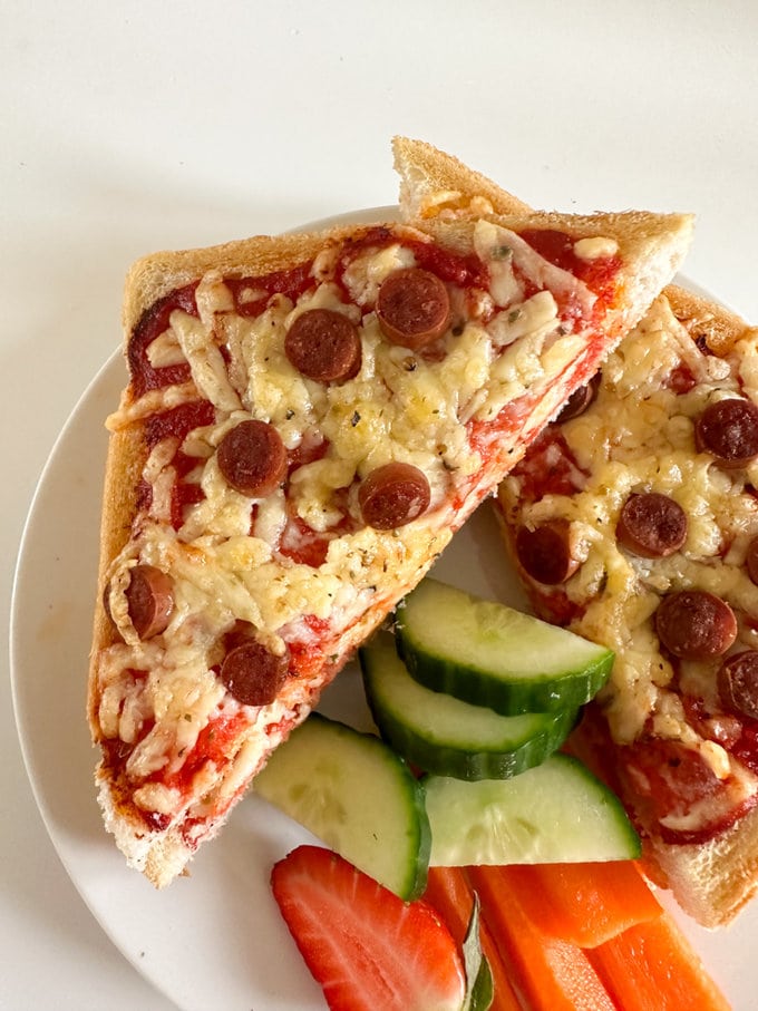 Airfyer Pizza Toastie cut in half and served on a plate with fresh sliced cucumber,carrot sticks and strawberries.