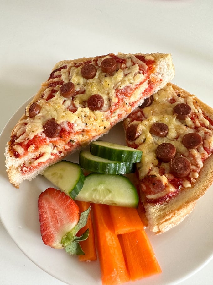Airfyer Pizza Toastie cut in half and served on a plate with fresh sliced cucumber,carrot sticks and strawberries.