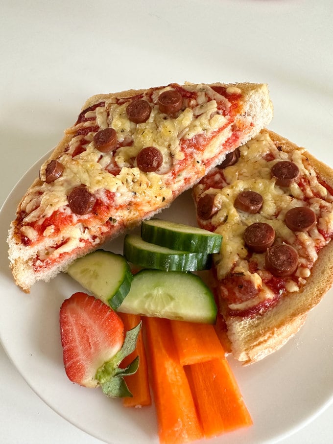 Airfryer Pizza Toastie cut into two triangles with carrot batons, sliced cucumber and strawberry served on white plate.