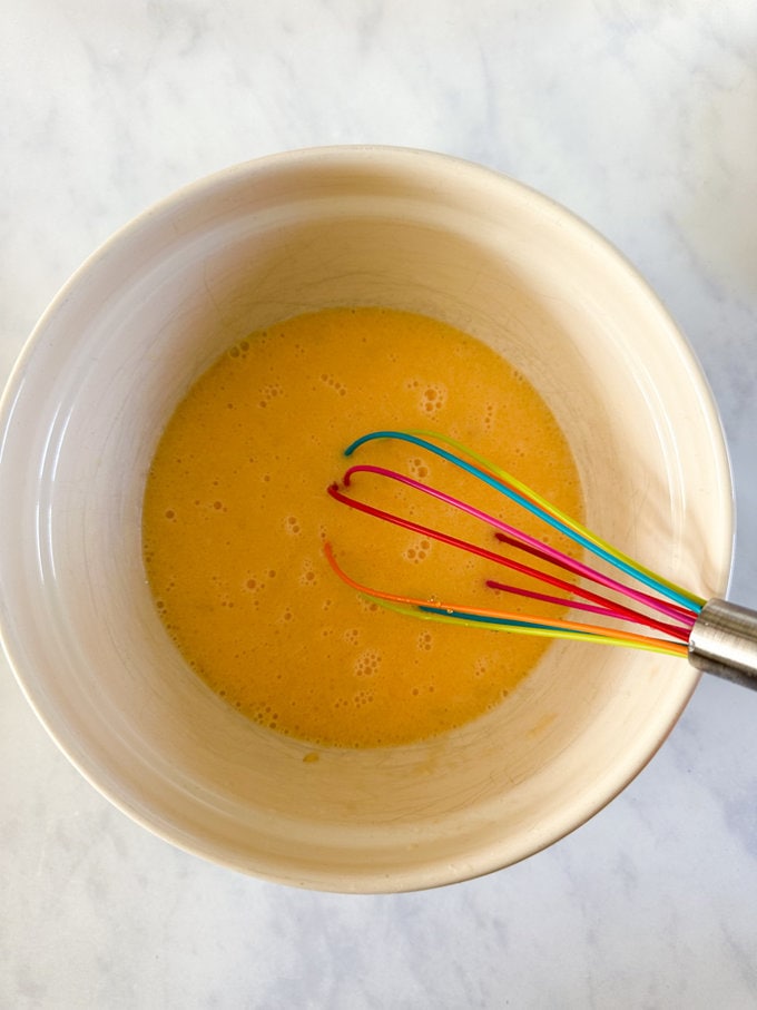 Ingredients being mixed together in a bowl with a colorful whisk. 