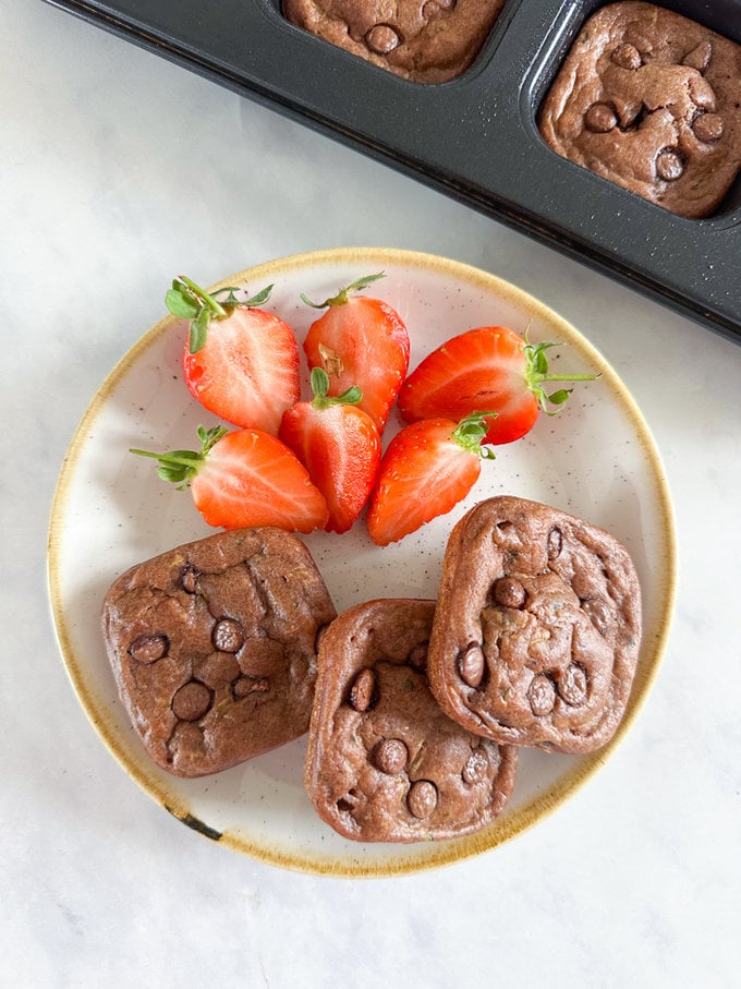 3 mini courgette banana breads served on a plate with chopped fresh strawberries.