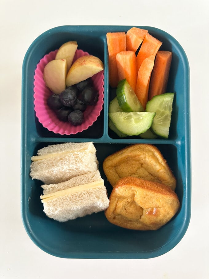 Mini Carrot Banana Bread served in  a divided lunch box along with a sandwich and fresh berries and cucumber. 