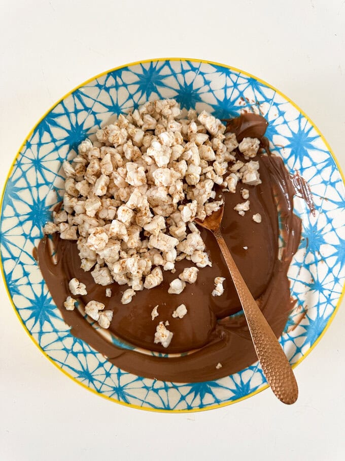 Ingredients for the Rice Cake Clusters being combined in a colorful blue and yellow bowl using a spoon.