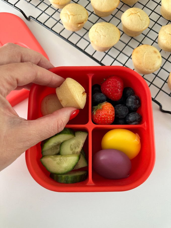 Mini Lemon Muffins in a red compartment snack box with fresh fruit and veggies and a couple or portion of mini babybel cheese.