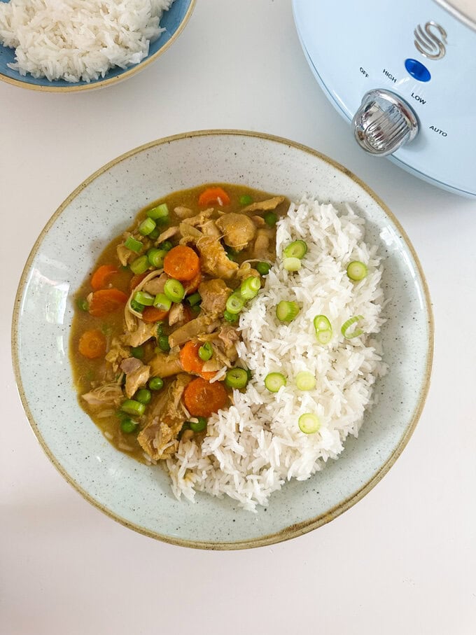 Slow Cooker Mayflower Chicken Curry served on a round white dinner plate, served with white fluffy rice and garnished with chopped spring onions.