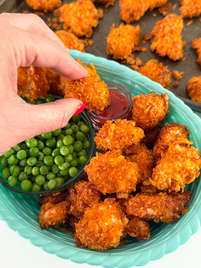 Crispy Cornflake Chicken Nuggets served in a blue basket style bowl along with a small bowl of garden peas and tomato ketchup for dipping.