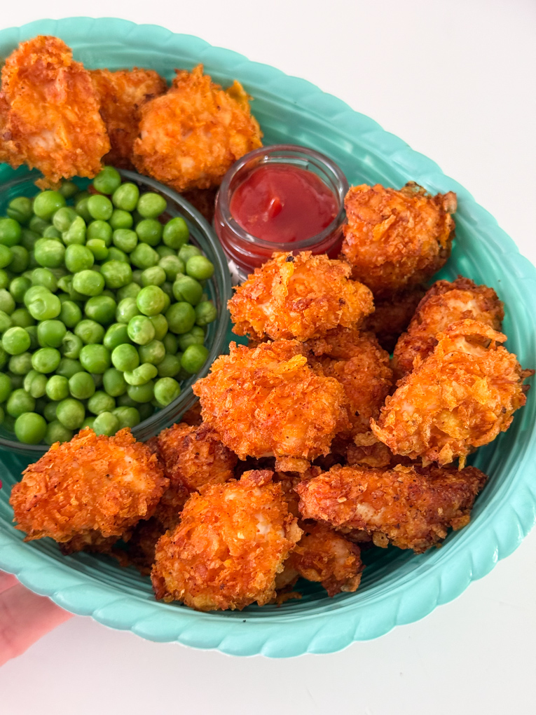 Crispy Cornflake Chicken Nuggets served in a blue basket style bowl along with a small bowl of garden peas and tomato ketchup for dipping.
