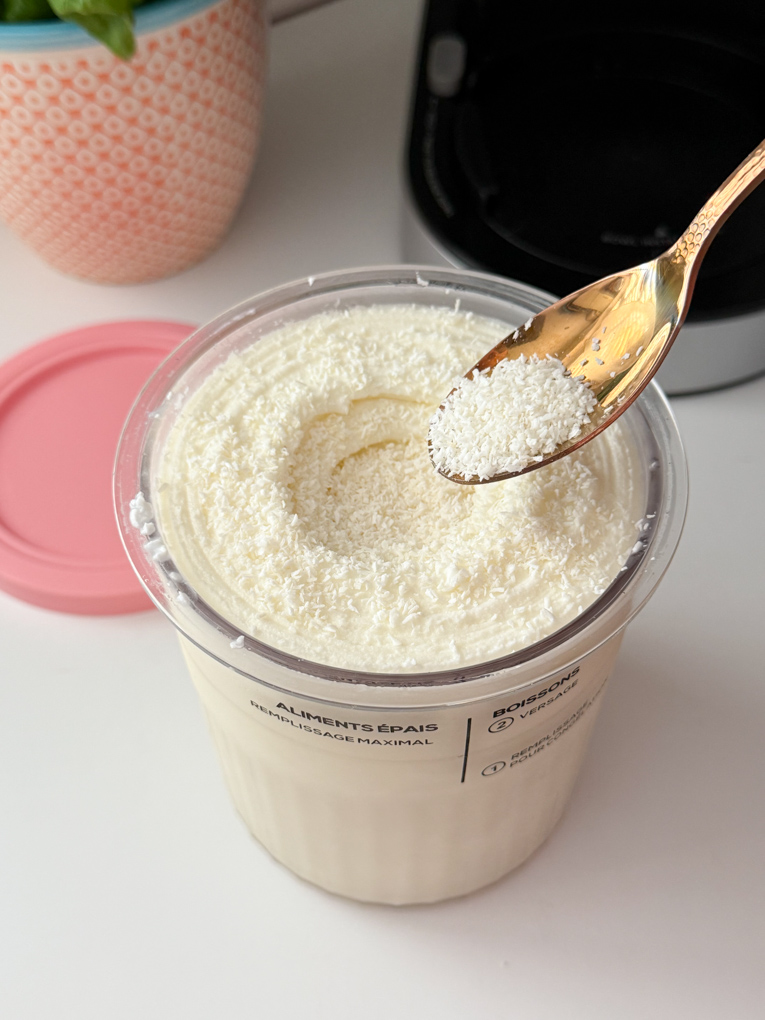 Ninja Creami Coconut Frozen Yogurt with coconut flakes being added into the top with a teaspoon.