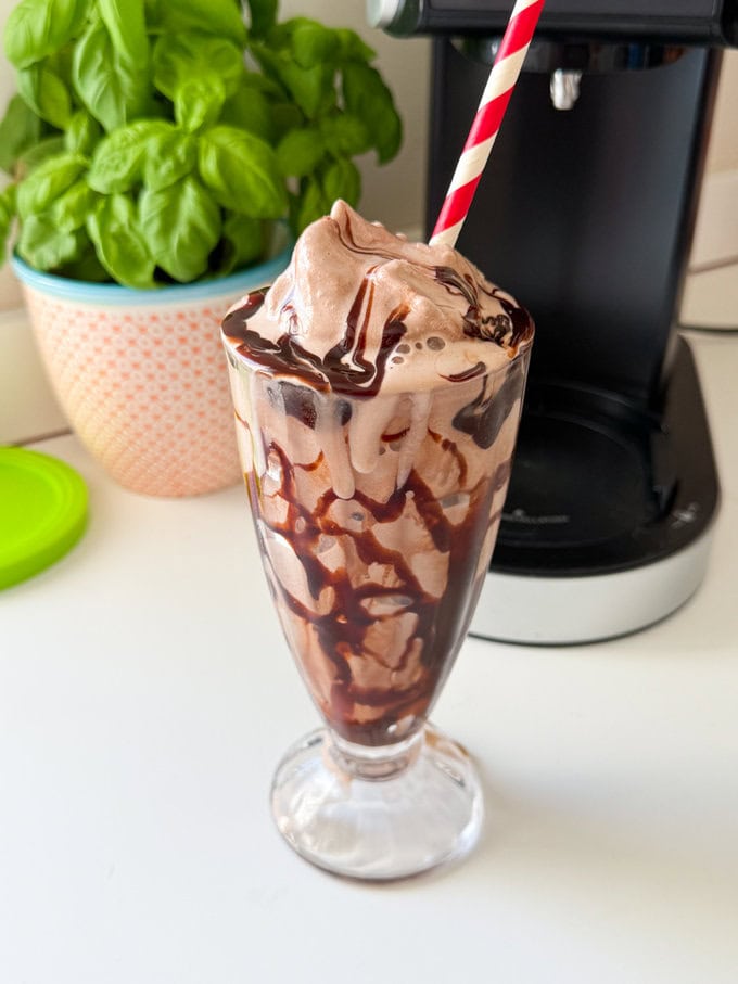 Ninja Creami Chocolate Milkshake served in a tall clear milkshake glass with a red and white striped straw.