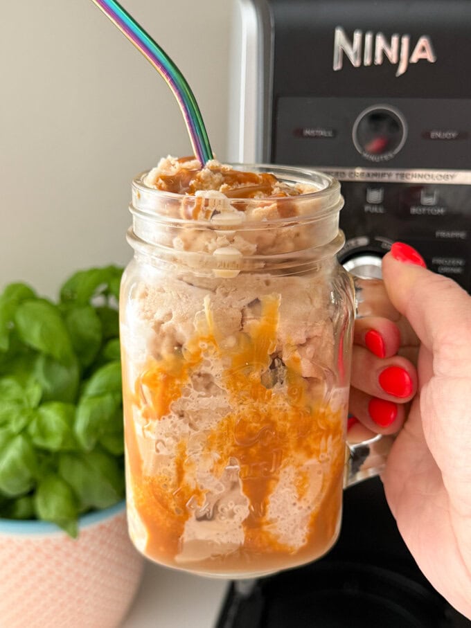 Ninja Creami Coffee Frappe served in a Milkshake glass drizzled with caramel sauce and a straw popped in the top.