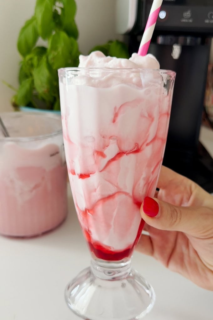 A tasty and easy frozen Strawberry Milkshake made in the Ninja Creami served in a tall clear milkshake glass with a pink and white straw for decoration.