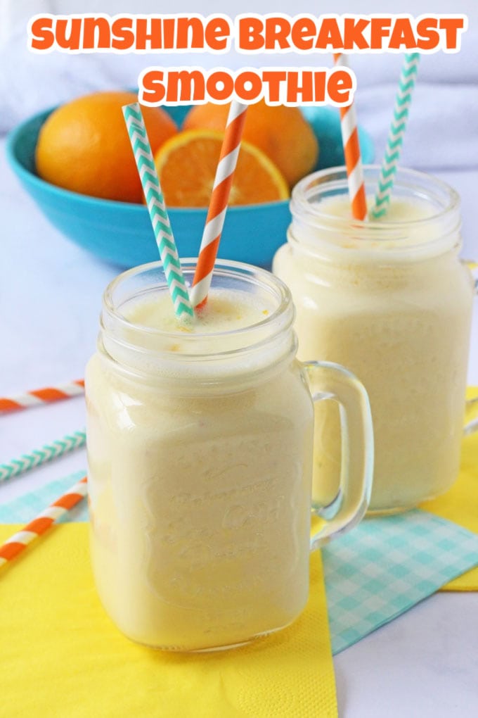 Two orange smoothies served in glass mason jugs with two brightly coloured straws in each jar and a bowl of oranges in the background.