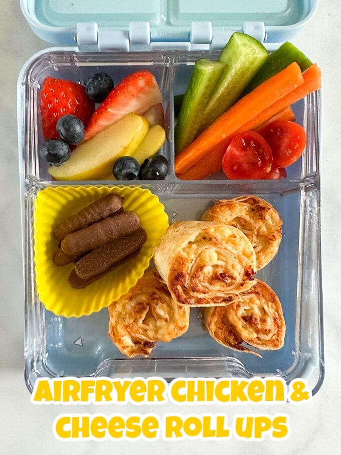 4 chicken and cheese pinwheels in a clear compartment lunchbox with fresh chopped fruit and veg and a small serving of mini chocolate fingers.