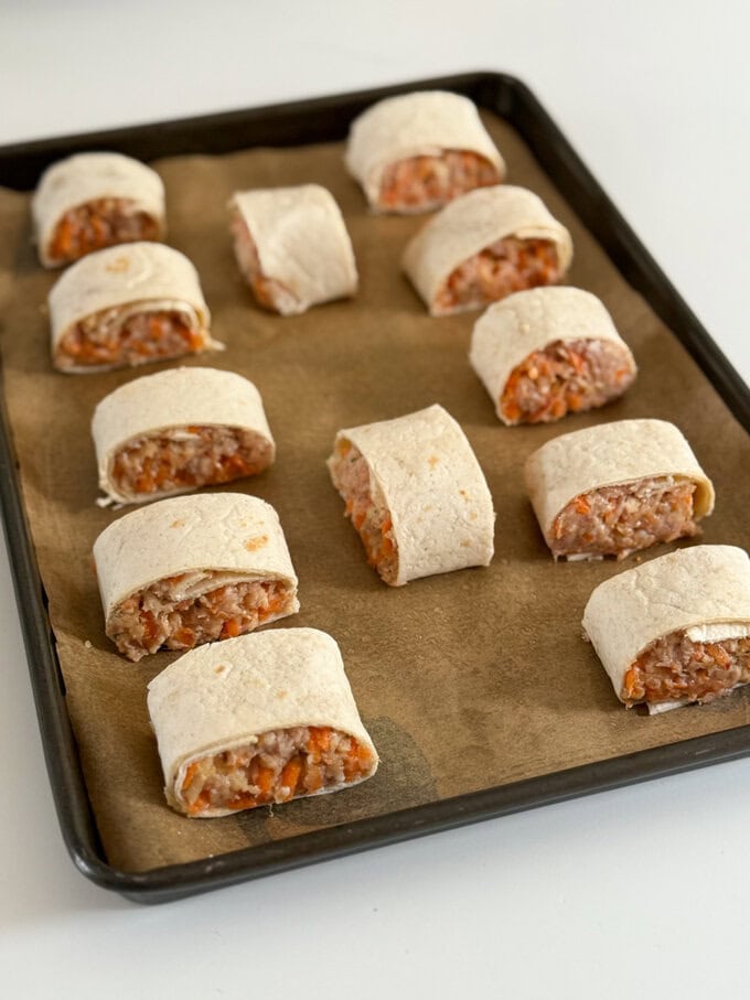 Apple & Carrot sausage rolls arranged on a baking tray ready to pop in the oven.