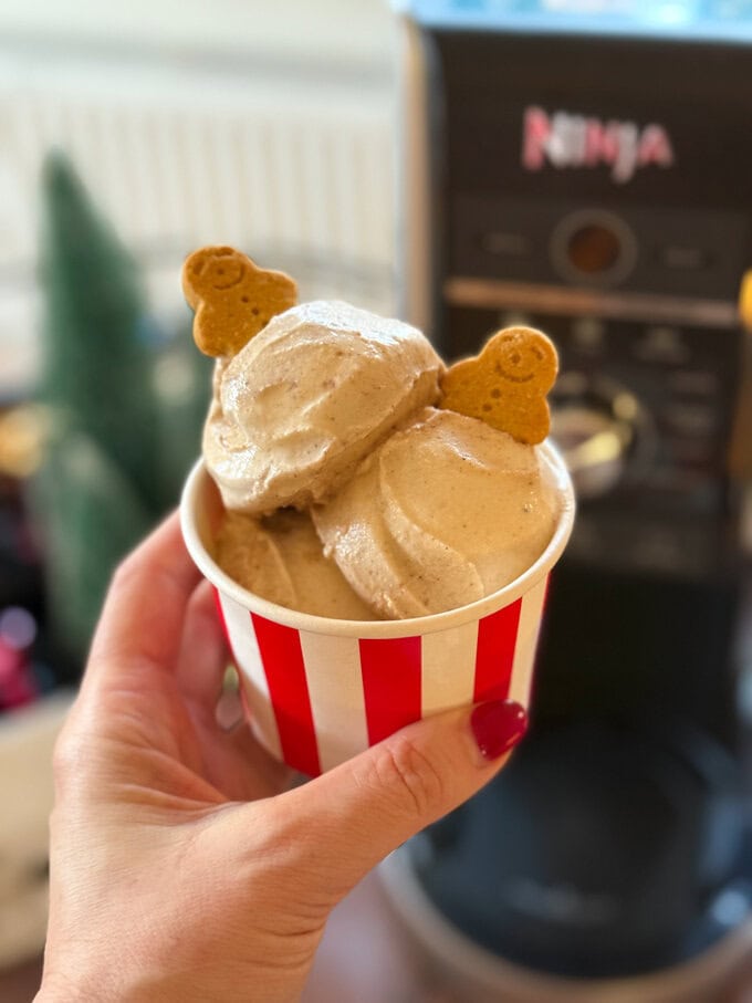 Three scoops of Ninja Creami Gingerbread Ice Cream, served in a red and white striped ice cream bowl and garnished with two mini gingerbread men biscuits.