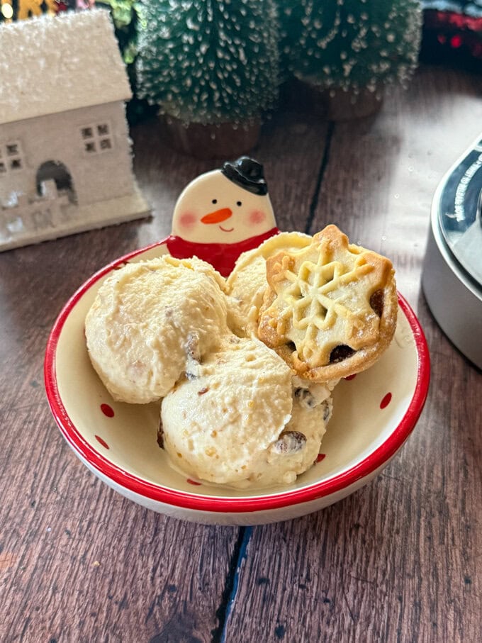 A festive snowman bowl with two large scoops of mince pie ice cream, with a mince on the side.