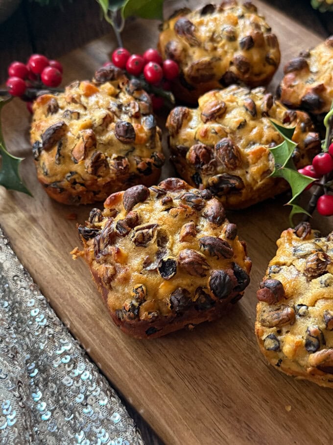 Mini Christmas cakes arranged on a wooden serving board decorated with holly and berries.
