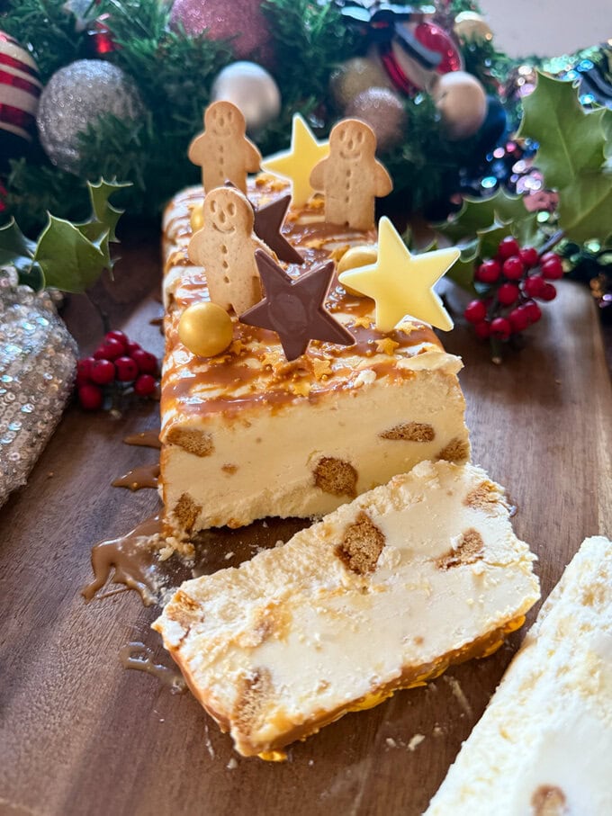 White Chocolate Semifreddo decorated with white chocolate stars,mini gingerbread men biscuits an drizzled with caramel sauce. sliced so you can see in inside.Surrounded by festive decor.