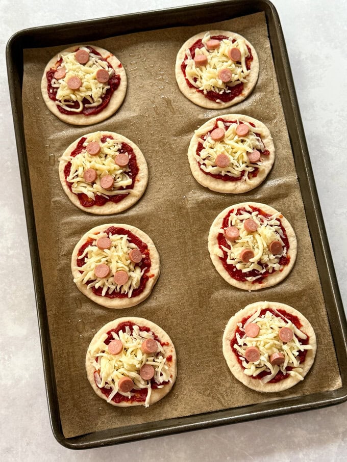 Mini pizzas arranged on a baking tray ready to pop into the oven for cooking.