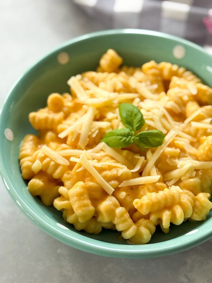 Butternut Squash Pasta served in a small turquoise bowl with white polka dots with a child's pink fork Garnished with grated cheese and sprig of fresh basil.