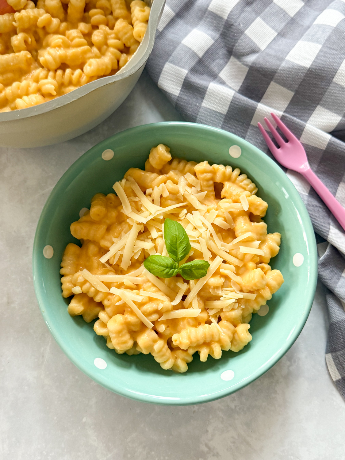 Butternut Squash Pasta served in a small turquoise bowl with white polka dots with a child's pink fork Garnished with grated cheese and sprig of fresh basil.