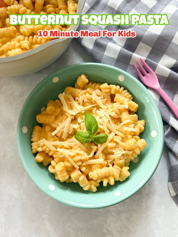 Butternut Squash Pasta served in a small turquoise bowl with white polka dots with a child's pink fork Garnished with grated cheese and sprig of fresh basil.