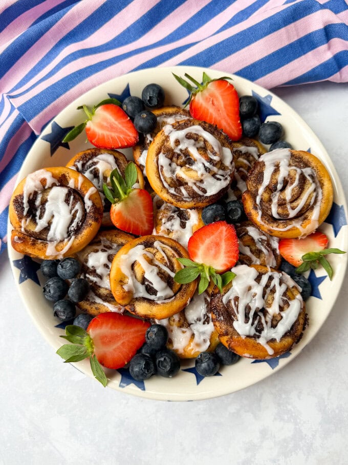 Petits pains à la cannelle disposés sur une grande assiette ronde et joliment décorés de fraises et de framboises hachées. 