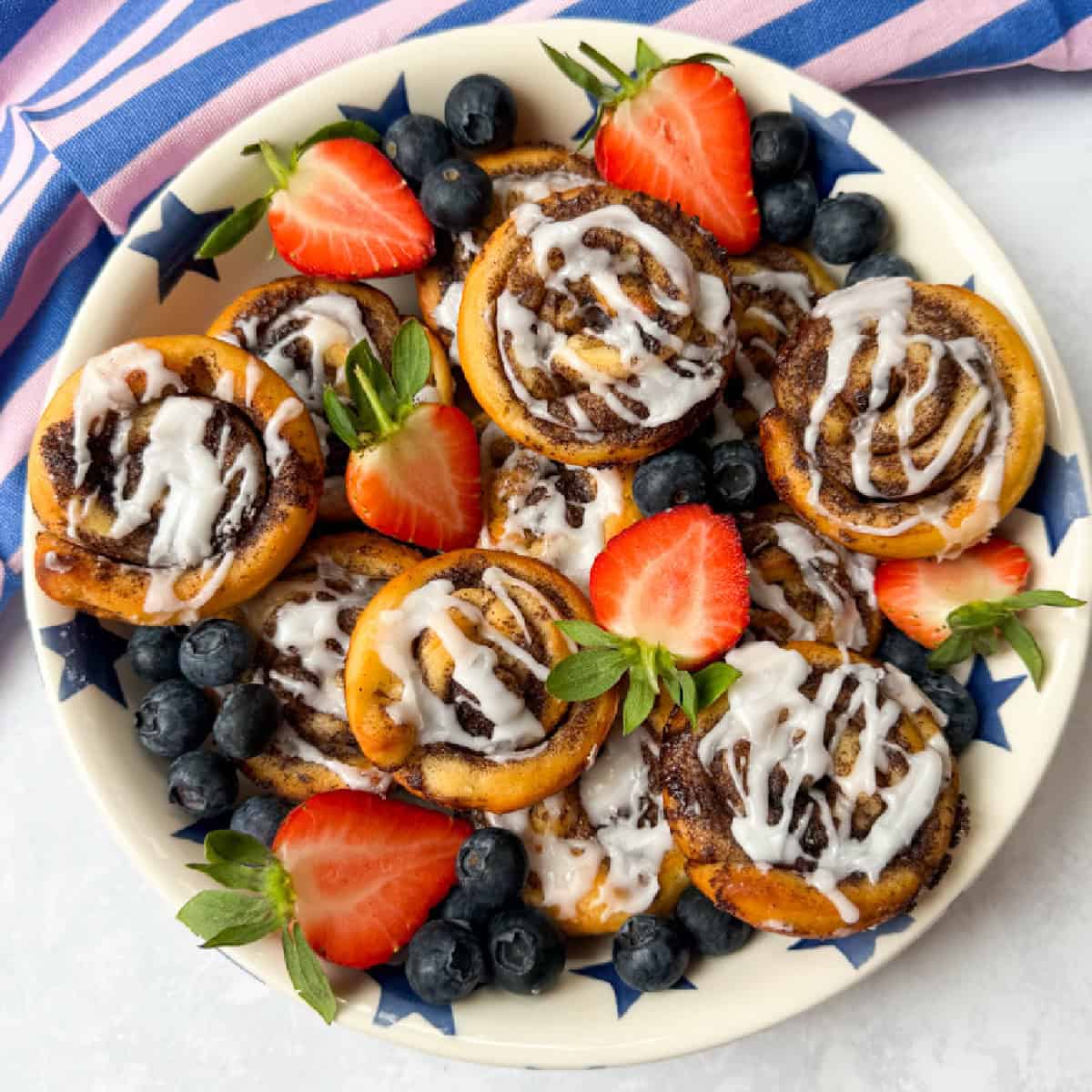 Cinnamon Rolls arranged on a large round plate and beautifully garnished with chopped strawberries and blueberries.