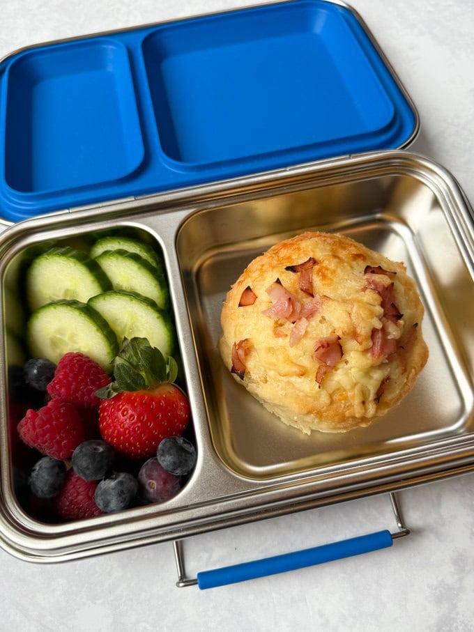 One Ham & Cheese roll in a childs lunchbox served with fresh fruit & veggies.