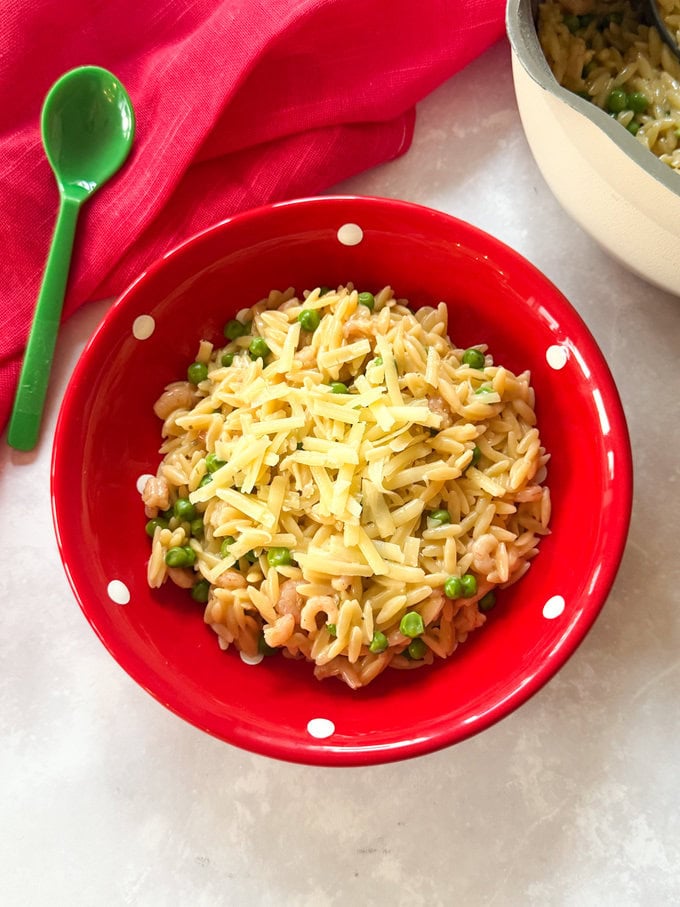 One Pot Prawn Orzo served in a small bright red bowl with white polka dots and garnished with grated cheese.