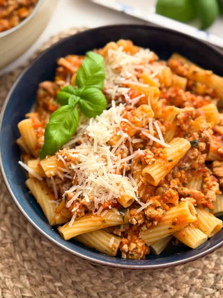Chicken mince bolognese in a large round dinner bowl garnished with grated cheese and a sprig of basil.