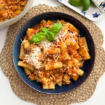 Chicken mince bolognese in a large round dinner bowl garnished with grated cheese and a sprig of basil.