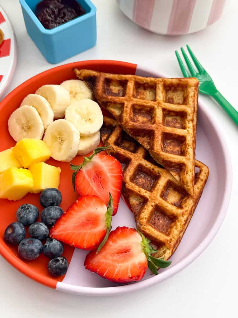 Porridge oat waffles served on a red and pink plate with fresh,chopped fruit.
