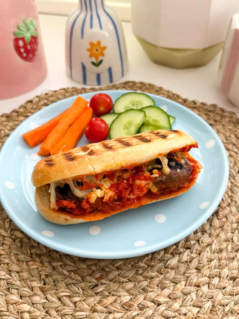 Meatball sub served on a baby blue round plate with white polka dots, along with fresh chopped veggies.