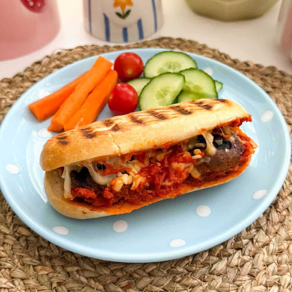 Meatball sub served on a baby blue round plate with white polka dots, along with fresh chopped veggies.
