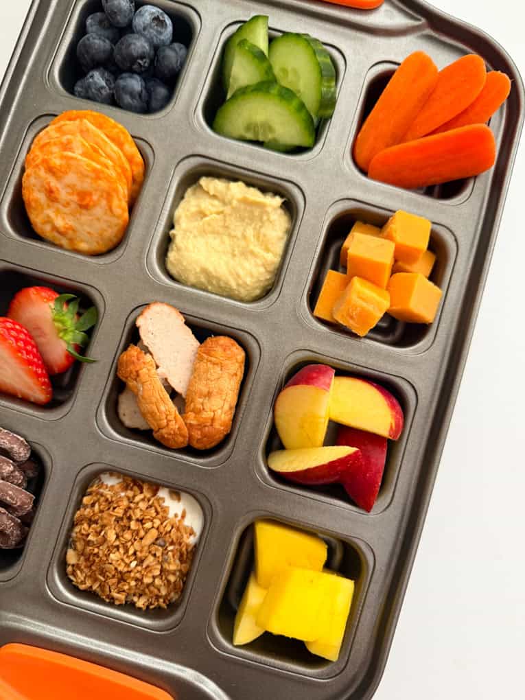 Verschiedene Snacks in einem quadratischen Muffinblech angeordnet. 
