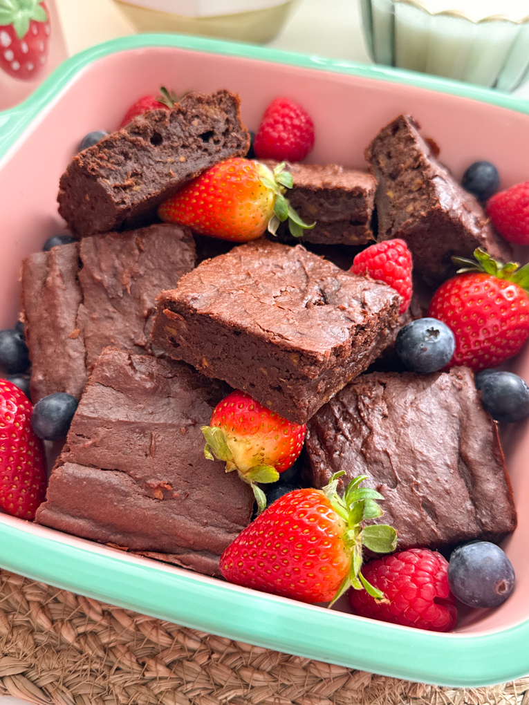 Brownies di patate dolci tagliati a quadrotti, serviti in una pirofila e guarniti con fragole intere e lamponi.