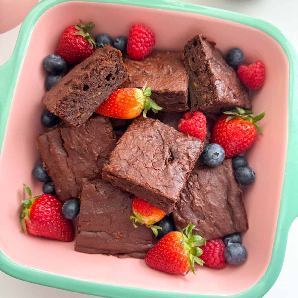 Sweet potato brownies cut into squares, served in a oven proof dish and garnished with whole strawberries and blueberries.