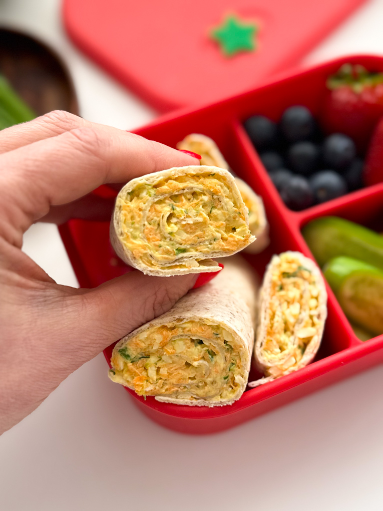 A close up photo of Veggie Cheese wraps served in a bright red child's lunchbox along with other lunchtime treats.
