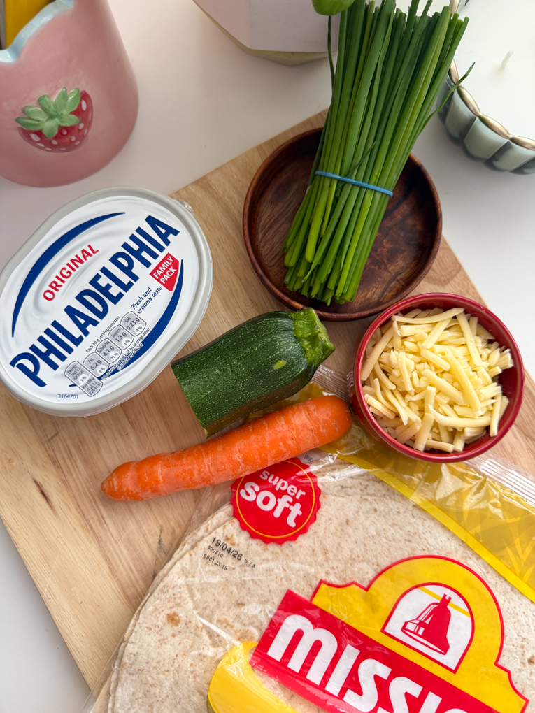 Ingredients to make veggie cheese wraps arranged on a wooden chopping board.