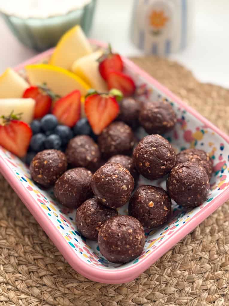 No Bake Chocolate Weetabix Bites presented in a rectangle bright coloured dish with chopped,fresh fruit.