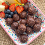 No Bake Chocolate Weetabix Bites presented in a rectangle bright coloured dish with chopped,fresh fruit.