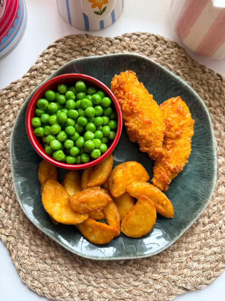 Cheesy chicken goujons on a dinner plate along with potato wedges and a small pot of garden peas.