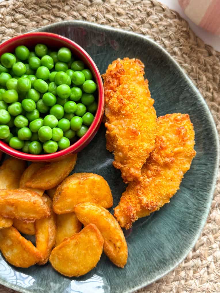 Cheesy chicken goujons on a dinner plate along with potato wedges and a small pot of garden peas.