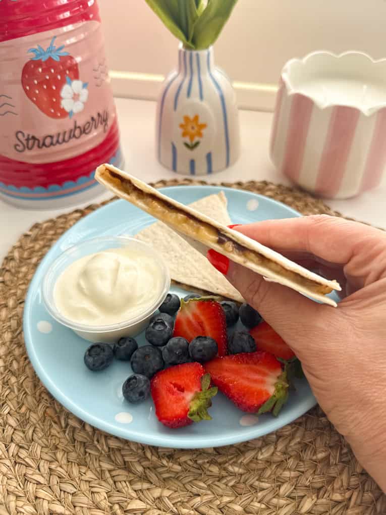Side profile of Chocolate banana wraps arranged on a baby blue coloured round plate with white polka dots and served with fresh berries and yogurt.