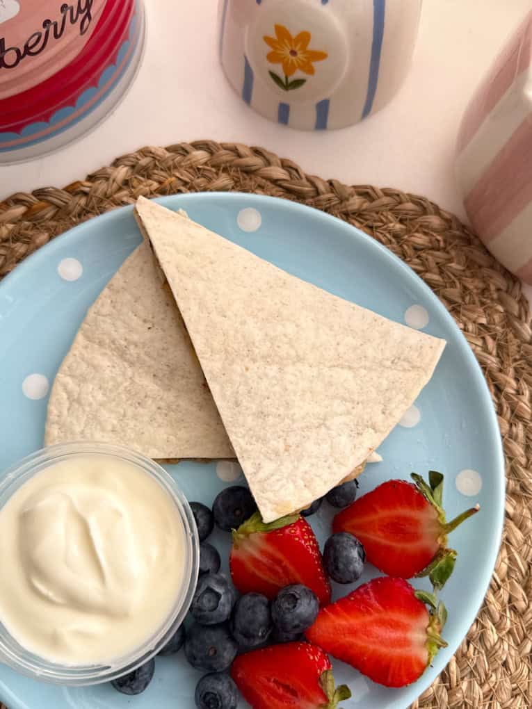 Chocolate banana wraps arranged on a baby blue coloured round plate with white polka dots and served with fresh berries and yogurt.