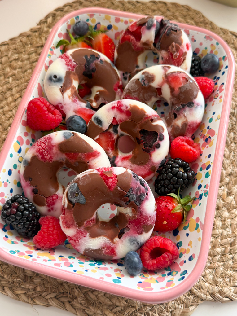Six frozen yogurt berry donuts in a pink spot patterned rectangle dish and garnished with fresh berries.
